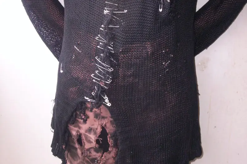 Close-up of a punk DIY garment constructed with interlocking safety pins holding torn fabric panels together